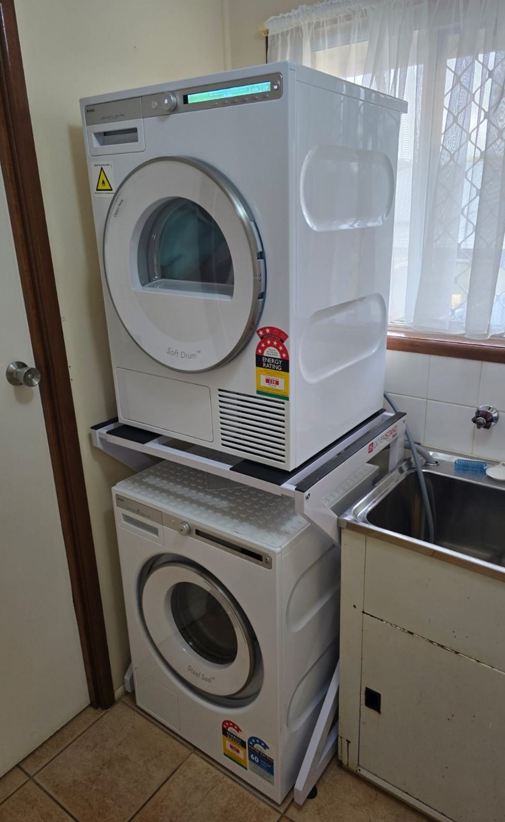 Real Space DryerStand Maxi showing a DryerStand freestanding tumble dryer stand in a real laundry space with a dryer above a washing machine